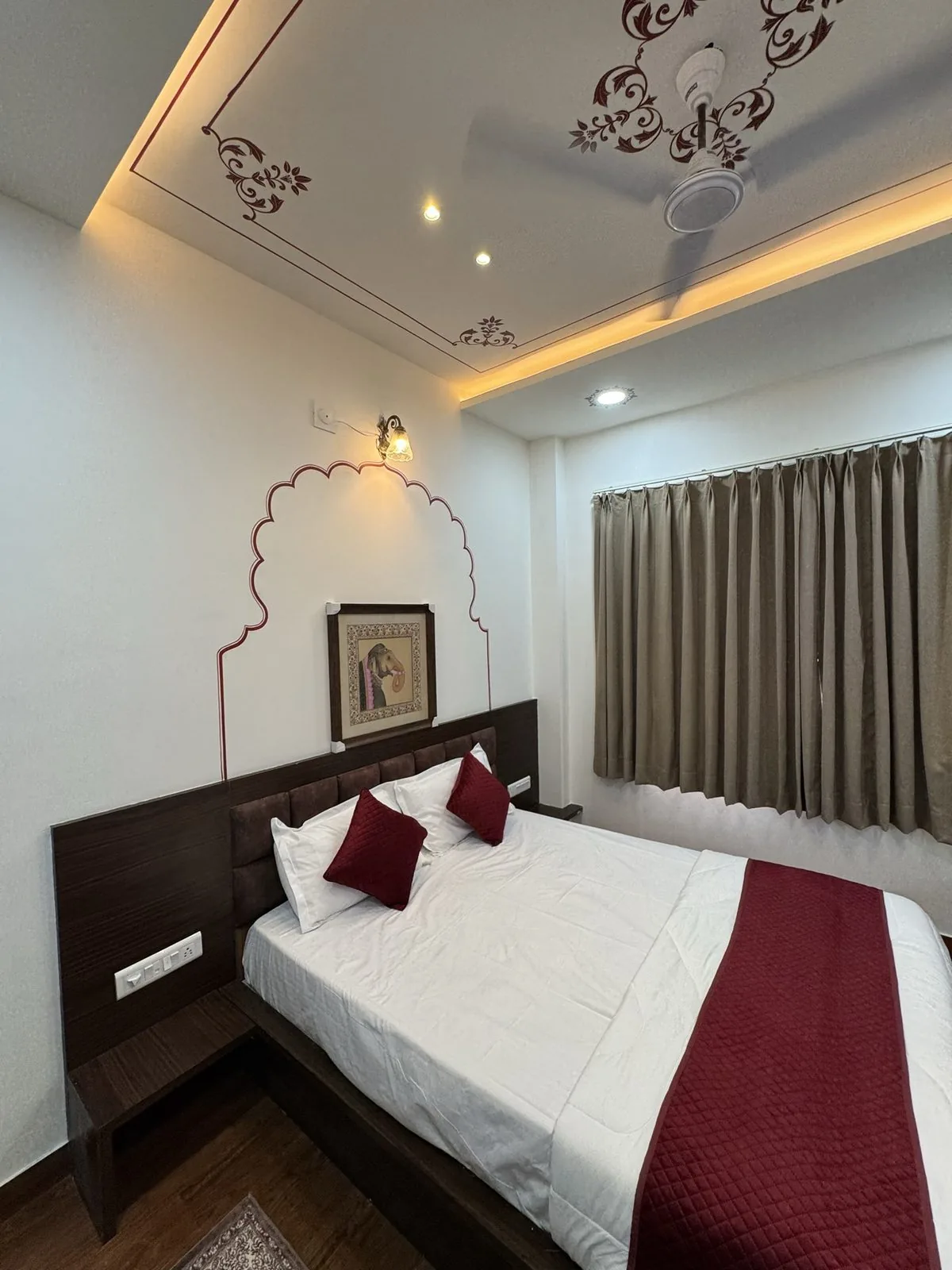 A guest room at Kalakar Haveli with a hand-painted scalloped arch, a framed miniature above the bed and a motif-painted ceiling